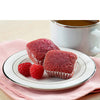 Two red velvet cupcakes on a plate with raspberries and a cup of coffee.